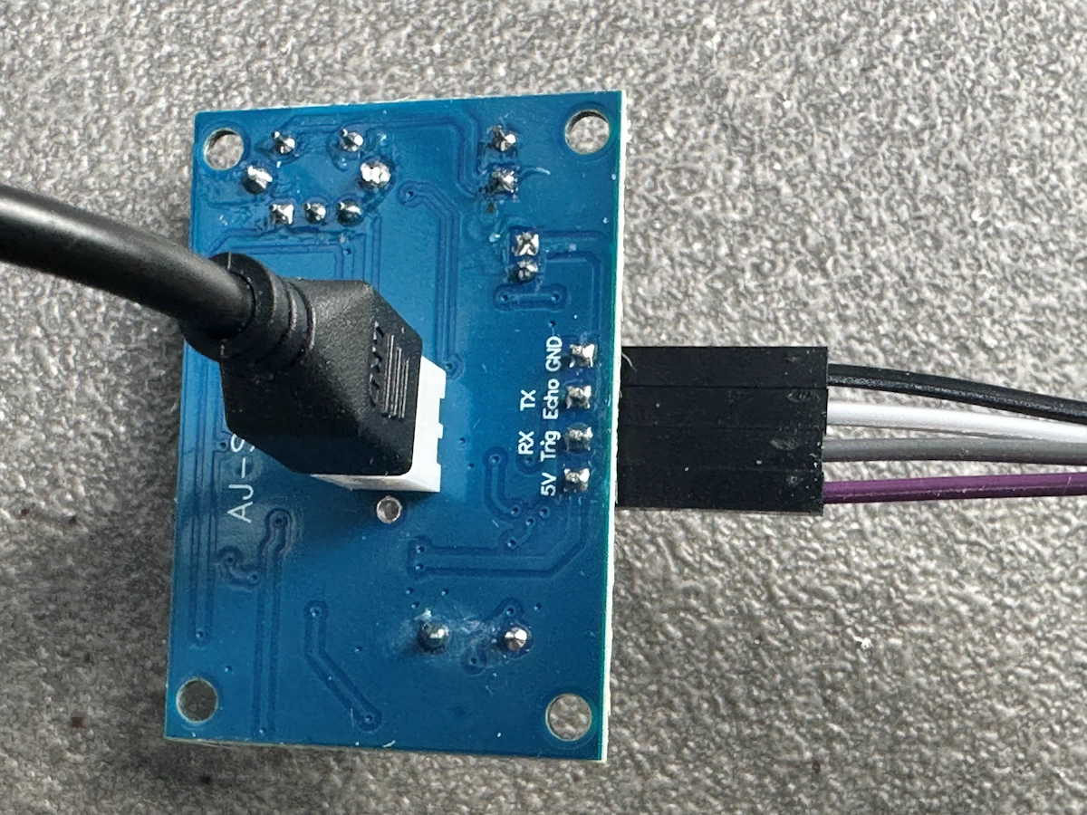 Anschlussleiste der JSN-SR04T-Steuerplatine mit violettem 5-Volt-Kabel, grauem Trigger-Kabel, weißem Echo-Kabel und schwarzem Massekabel