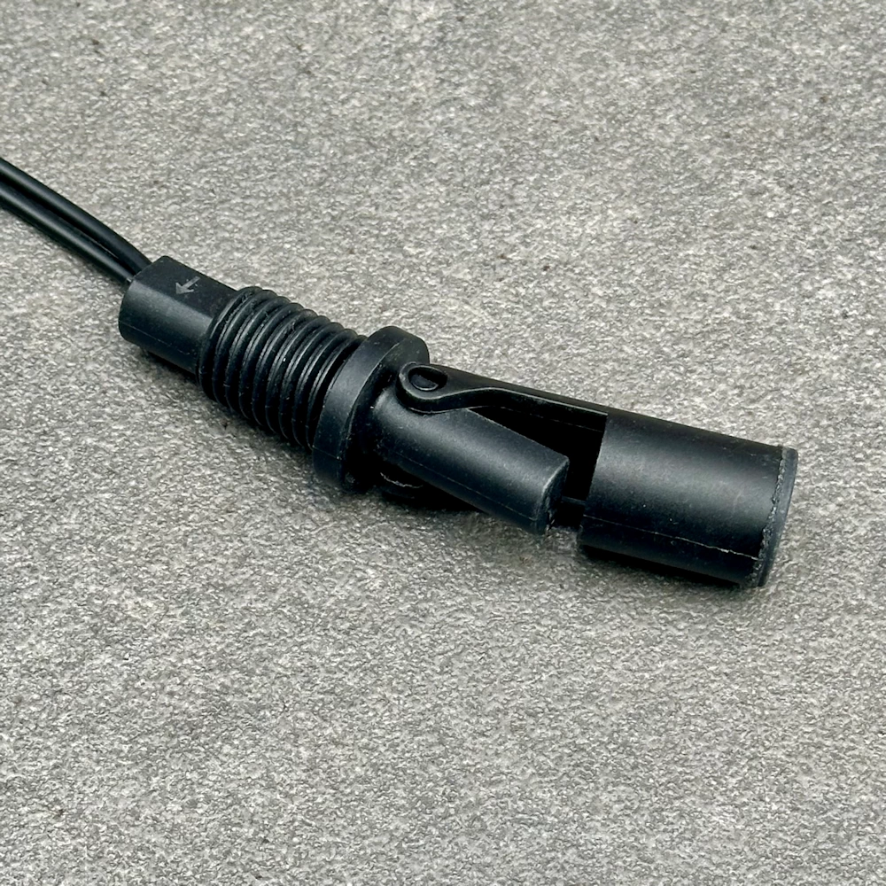 Nahaufnahme eines horizontalen Schwimmschalter-Sensors aus schwarzem Kunststoff mit Montagegewinde und Dichtung auf grauem Grund
